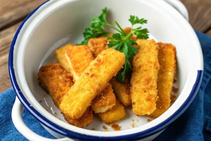 Goldbraune, knusprige fischstäbchen im airfryer, serviert in einer weißen Emaille-Schüssel mit Petersilie.