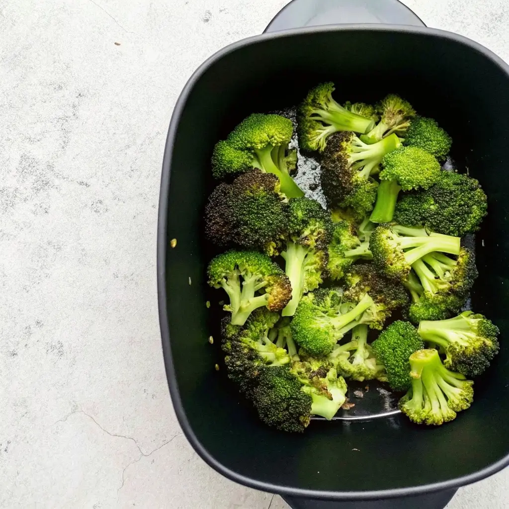 Brokkoli in einer schwarzen Airfryer-Schale, bereit für das Backen. Die Blumenkronen sind frisch und grün, mit einigen bereits knusprigen Rändern.