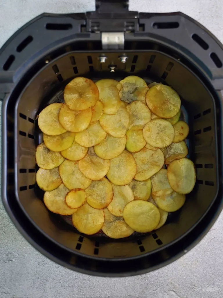 Geschnittene Kartoffeln mit Öl und Gewürzen in der Airfryer-Korb gefüllt – bereit für das Backen zu knusprigen Chips.
