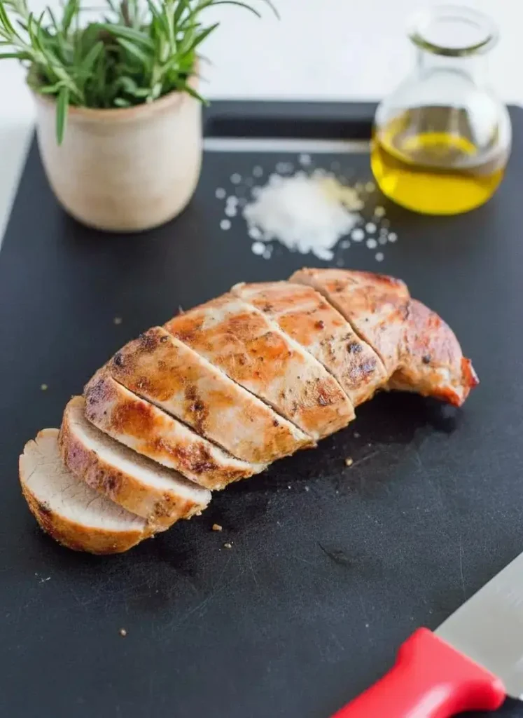 Geschnittenes Schweinefilet auf schwarzer Platte – so servieren Sie es perfekt nach dem Garen in der Heißluftfritteuse, garniert mit Rosmarin und Olivenöl.