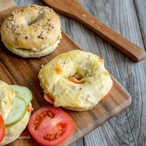 Frische Bagels mit Käse, Tomate und Gurke auf Holzbrett serviert – perfekt für Frühstück oder Snack