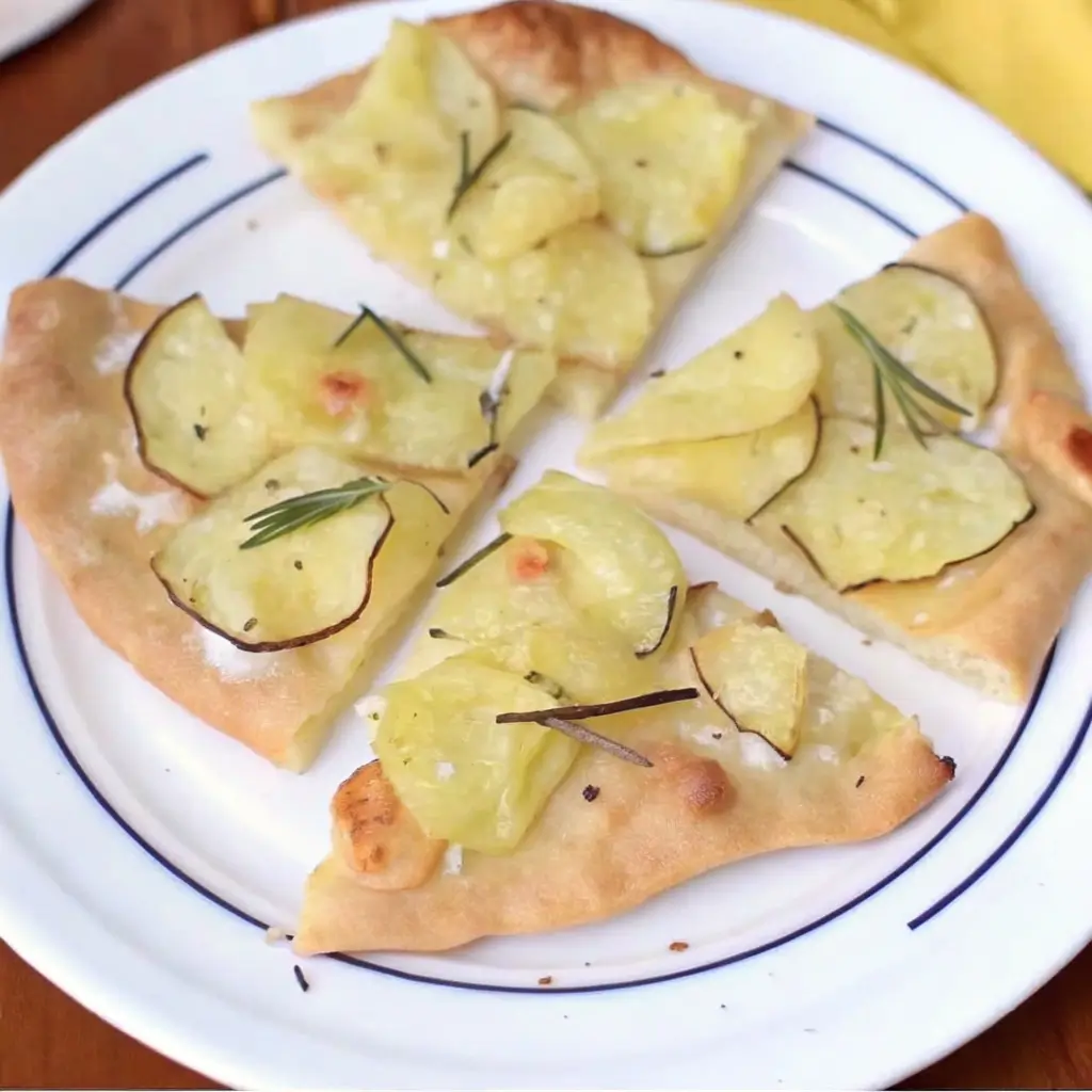 "Kartoffelpizza servieren - knusprige Pizza mit Kartoffelscheiben und Rosmarin auf Tellerstücken angerichtet"