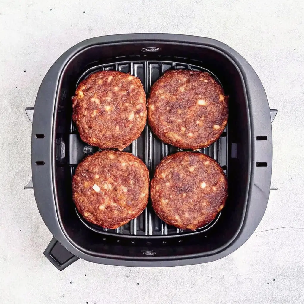 Burger aus dem Airfryer: Vier saftige Rindfleisch-Patties goldbraun gegrillt auf Grillrost im schwarzen Airfryer-Korb