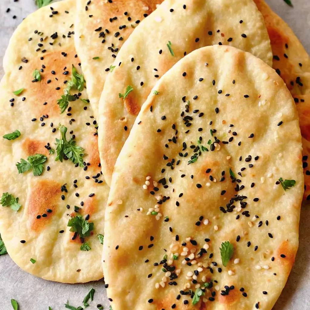 Naan Brot servieren: Mehrere goldbraune indische Fladenbrote mit schwarzem und weißem Sesam sowie Kräutern bestreut, kunstvoll gestapelt